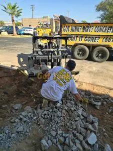 Worker breaking and removing concrete debris in Lancaster, CA ? rubble cleanup in progress with branded shirt visible.